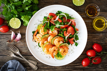 Fried shrimps with garlic, lime and fresh vegetables served on white plate on wooden table

