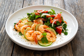 Fried shrimps with garlic, lime and fresh vegetables served on white plate on wooden table
