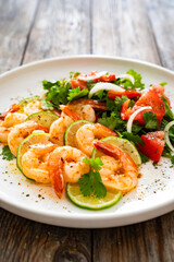 Fried shrimps with garlic, lime and fresh vegetables served on white plate on wooden table
