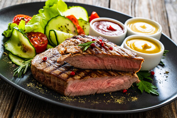 Grilled beef steak with sauces and fresh vegetables on wooden table