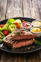 Grilled beef steak with sauces and fresh vegetables on wooden table