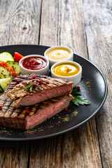 Grilled beef steak with sauces and fresh vegetables on wooden table