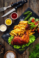 Oven roasted chicken thigh with French fries and fresh vegetables on wooden table
