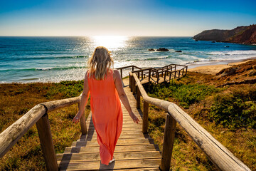 Beautiful woman walking on cliff to sunny beach Portugal, Algarve, Amado praia