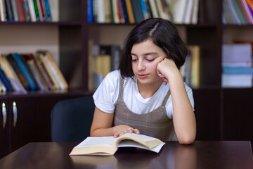 Beautiful schoolgirl sitting in the library and reading a book