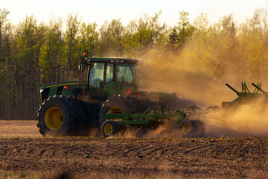 Grande Prairie, Alberta, Canada - May 10, 2024: John Deer heavy duty tractor 9460R with attached 1910 Air drill is seeding in the field in dust in the sunset.