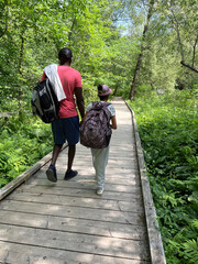 Vue arrière d'un père afro-américain et de sa fille marchant sur un chemin en bois dans la forêt