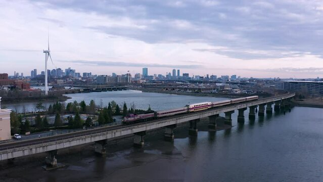 A train passes along the Mystic River Bridge in Everett, Massachusetts during sunset in front of the Boston skyline.