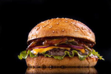 Burger with beef, cheese, vegetables on black plate. Dark Background. Close up.