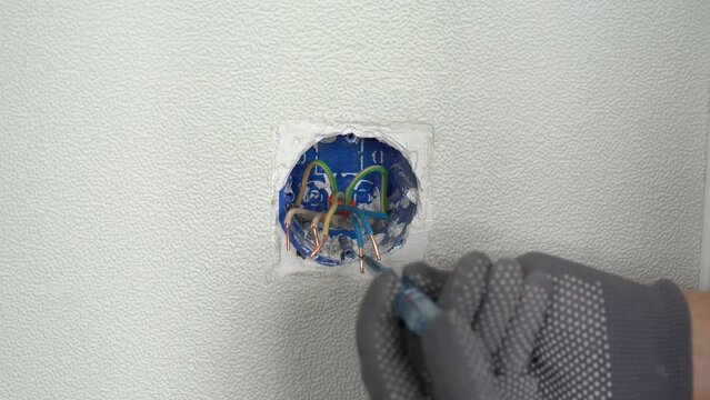Hands of electrician check current in open junction box with electrical wires using indicator screwdriver. Checking for faults in electrical socket. Replacing electrical outlet. Installing