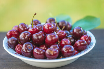 Bowl with ripe red cherries on a wooden table outdoors