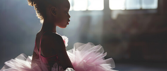A young ballerina in a soft, pink tutu stands contemplatively in a softly lit space, exuding innocence, grace, and early dedication to the art of dance.