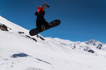 A woman snowboarder makes a ski jump against the backdrop of high snow-capped mountains