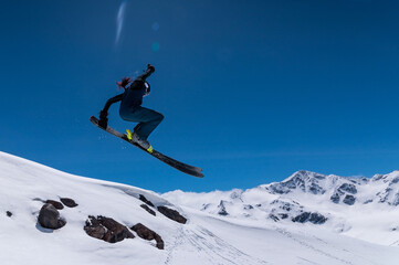 A woman skier makes a ski jump against the backdrop of high snow-capped mountains. Ski resort. winter sports