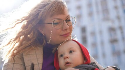Slow motion. Close-up. A mother hugs her little son and gently kisses his forehead, sitting in a sunny spring day in the yard of an apartment complex. Low-angle shot - Powered by Adobe