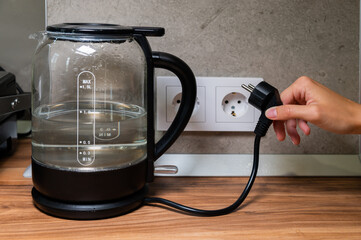 glass modern electric kettle stands on the table against the background of an outlet. Boiling...