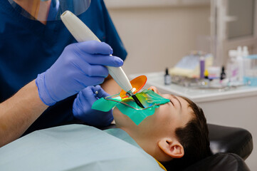 The dentist dries the filling for the child using a polymerization lamp. A cofferdam is installed...