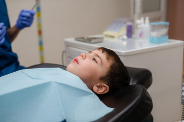 A cute little boy in a dental chair treats his teeth, smiling and happy