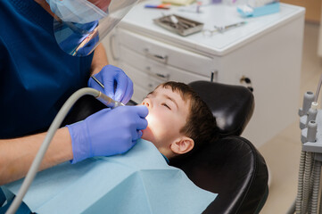 The dentist checks teeth of boy who is sitting in a dental chair. Dental treatment. - Powered by Adobe