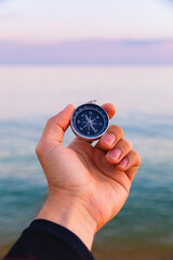 Navigation compass in a man's hand against the background of the sea, tourist compass first person view