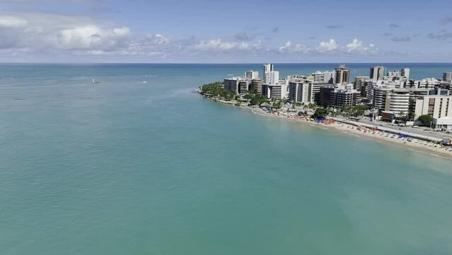 Drone flies backwards from Praia Jatiuca over emerald green ocean water on a sunny afternoon in Maceio, Alagoas, Brazil