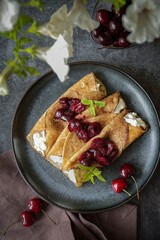 Crepes with ricotta cheese served on the plate with blueberries, strawberries and cherries