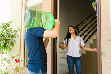 Delivery man carrying a heavy water jug and a smiling woman greeting him at the entrance of a house