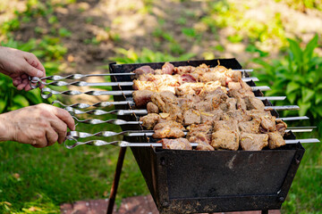 Grilling Meat Skewers on a Sunny Day. Close-up of hands turning meat skewers on a grill outdoors on a sunny day.