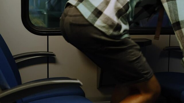 A young traveler guy with a backpack sits on an empty seat in a train carriage. Travel alone concept