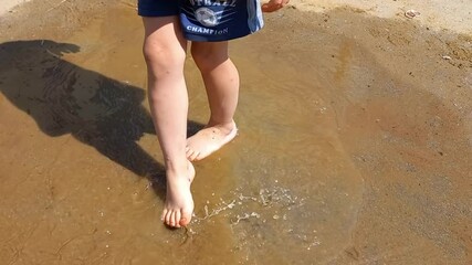 4 year old boy runs through a puddle barefoot after the rain