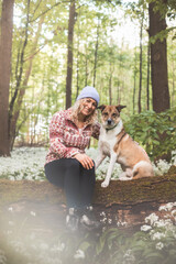 Cute blonde cuddles with her dog on a tree trunk surrounded by bear garlic. Relationship between woman and dog. Trust, love and tenderness