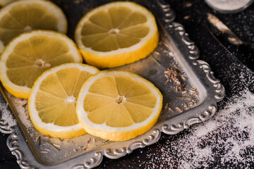 Lemon slices on a silver tray with a knife and a small jar of salt on a dark background with dramatic lighting in the style of dark food photography.