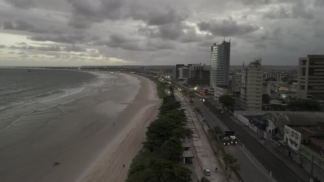 Drone flies along Avenida da Praia beach and coastal highway on overcast day just before sunset
