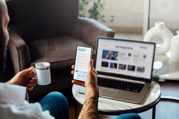 Man looking at calendar on mobile phone early in the morning for planning the day. News site on the laptop screen. Digital schedule concept.