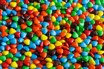 Colorful sweet little glazed multicolored chocolate bonbons candies, m and m's with heart shapes, full frame background