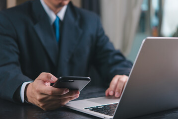 Businessman using phone and laptop simultaneously. Concept of multitasking, modern work environment, professional communication. Ideal for corporate, business settings.