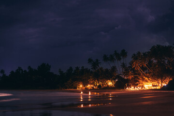 Nighttime Beach Scene with Illuminated Palm Trees and Reflections