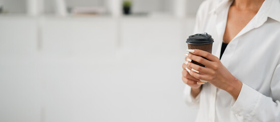 Close-up of a woman holding a coffee cup in a modern minimalist setting, wearing a white shirt with manicured nails.