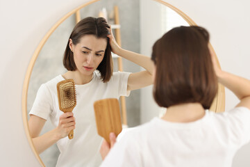 Sad woman holding brush with lost hair indoors. Alopecia problem