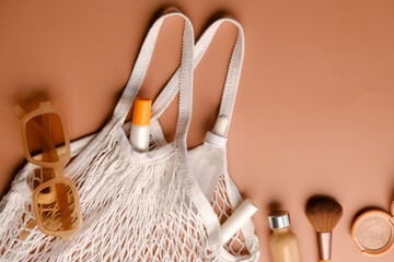 A collection of personal items for a beauty or skincare routine, including a white mesh tote bag, cosmetics or skincare products, sunglasses, makeup brushes, and bottles.