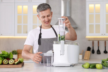 Smiling man with fresh products using juicer at white marble table in kitchen