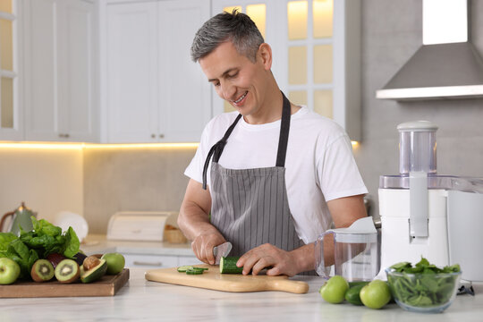 Juicer and fresh products on white marble table. Smiling man cutting cucumber in kitchen - Powered by Adobe