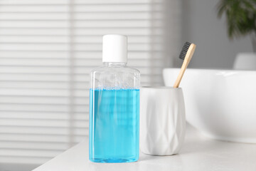 Bottle of mouthwash and toothbrush on white countertop in bathroom