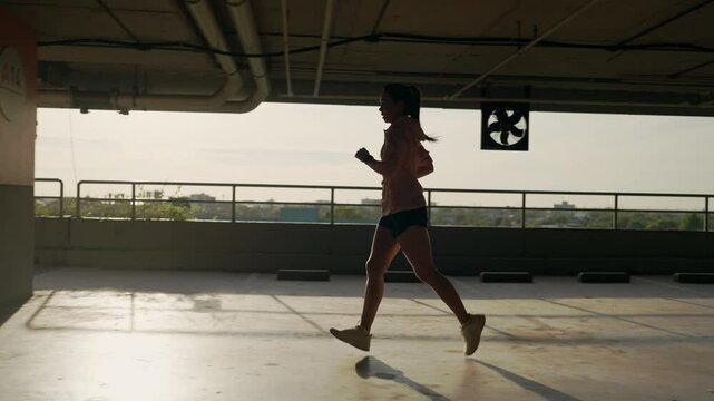 A woman is running on a concrete floor with a fan in the background. The fan is turned off and the woman is the only person in the image