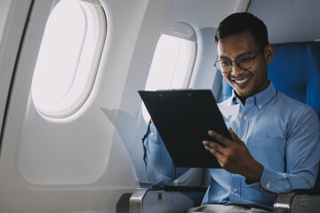 Attractive Asian male passenger of airplane sitting in comfortable seat while working laptop and tablet with mock up area using wireless connection. Travel in style, work with grace.