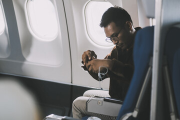 Happy curly man use phone and listens to music headphones on board airplane during flight.