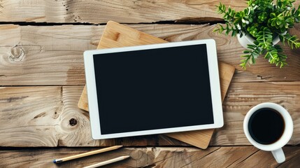 Blank screen tablet on wooden office desk with coffee pencil and plant