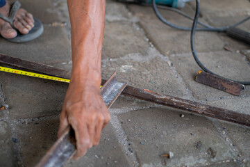 Person measuring metal bar with tape measure