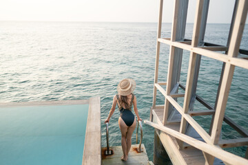 Woman in black swimsuit relaxing by infinity pool with ocean view.
