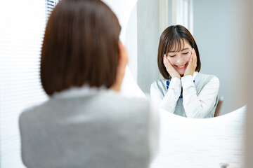 鏡の前で肌を触り笑顔の女子高生